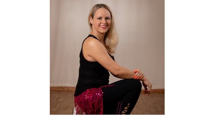 Kvinna sitter på huk i danskläder med röd kjol och svart linne i ett rum med trägolv.