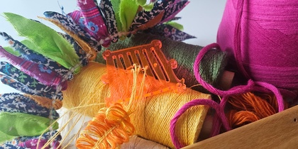 Närbild av färgglada sytrådar, garn, tygbitar och ett vävverktyg på ett bord.