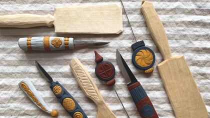 Flera handgjorda träsnideriverktyg och knivar med dekorerade handtag ligger på en randig tygduk.