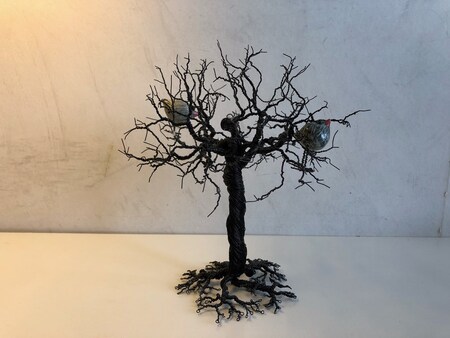 En konstgjord trädskulptur av svart metalltråd med två små dekorationer i grenarna.
