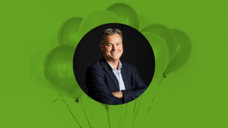 Man i kostym ler mot kameran, omgiven av gröna ballonger på grön bakgrund.