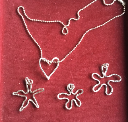 Smycken av silvertråd på röd sammet, inklusive ett hjärthalsband och tre stjärn- och blomformade hängen.