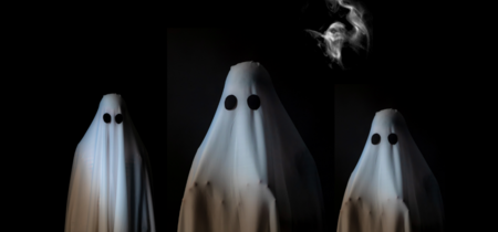 Tre personer utklädda till spöken med vita lakan och svarta ögon på en mörk bakgrund.