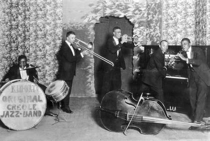 Ett jazzband med fem musiker spelar instrument på en scen, svartvit bild från tidigt 1900-tal.