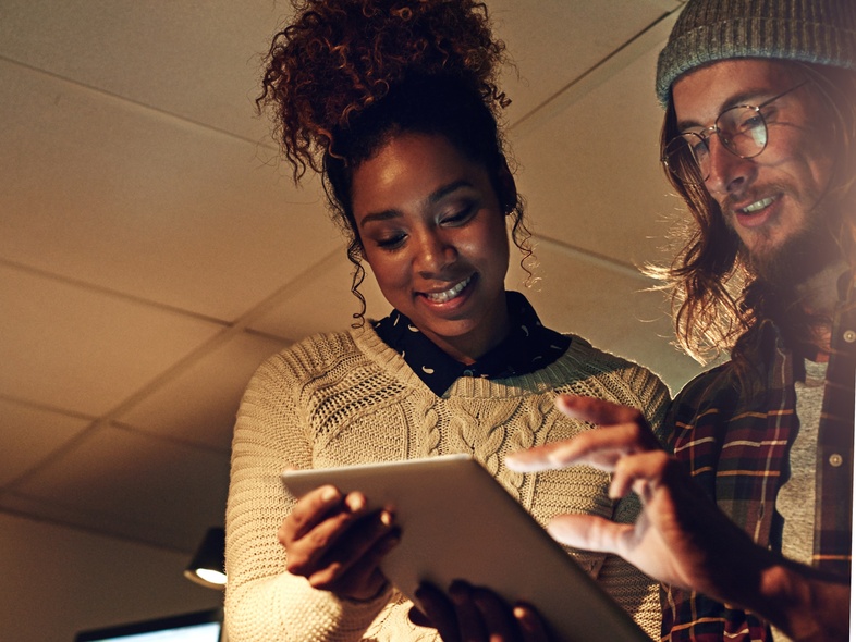 Två personer samarbetar vid en surfplatta i ett kontorsutrymme med dämpad belysning.