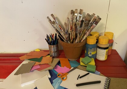 Ett bord med konstmaterial som penslar, färg, papper, svampar, sax och färgpennor.