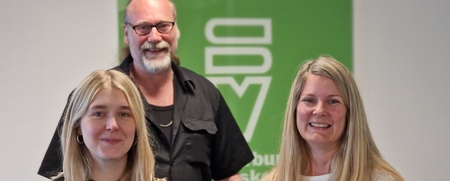 Tre personer står framför en grön skylt och ler mot kameran.