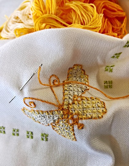 Närbild av korsstygnsbroderi med en gul fjäril, nål och gult broderigarn.