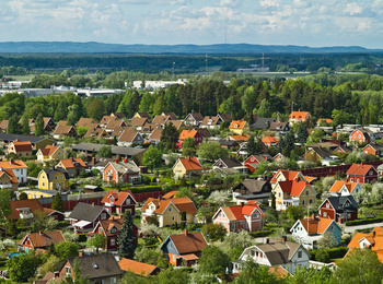 Färgglada villor med röda och gula tak i ett grönt bostadsområde, omgivna av träd och skog.