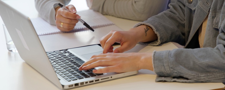 Två personer sitter vid ett bord, en skriver på en laptop och den andra antecknar i ett block.