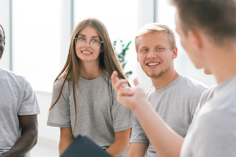 En grupp unga vuxna sitter tillsammans och samtalar, alla bär grå t-shirts.