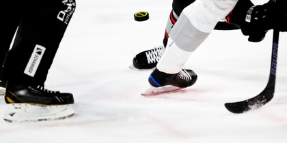 Närbild på ishockeyspelare som kämpar om pucken på isen under en match.