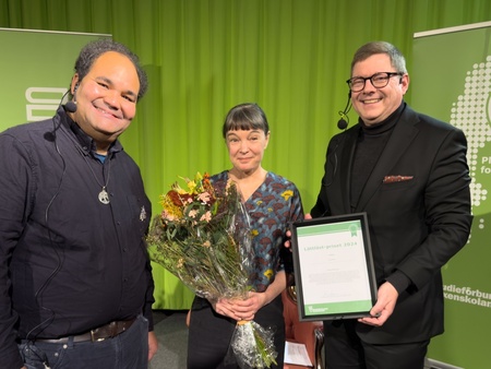 Quinten Moody, Lisa Förare och Per Lodenius står framför en grön bakgrund, Lisa håller en blombukett och Per ett diplom.