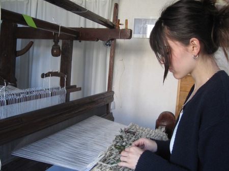 En person arbetar vid en vävstol och väver tyg i ett rum med ljusa väggar.