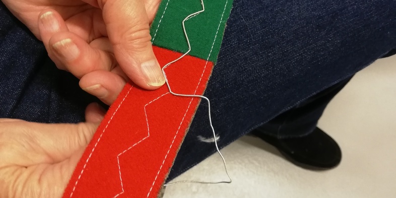 En person syr för hand på ett färgglatt band med röd, grön, gul och blå sektion.