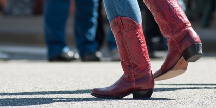 Person i blå jeans och röda cowboyboots dansar utomhus på asfalt.