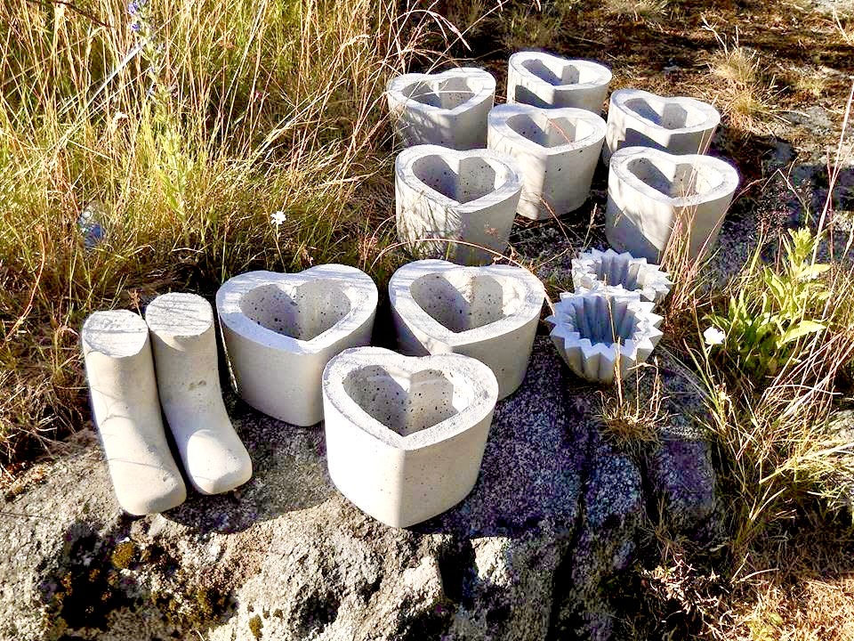 Betongformar i hjärtform och stövelform står på marken bland gräs och stenar utomhus.