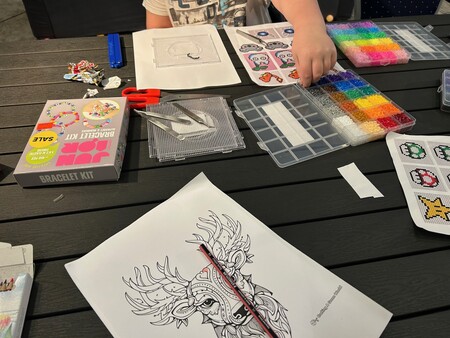 Ett bord med pärlplattor, färgglada pärlor, armbandssats, sax och en teckning av en hjort.