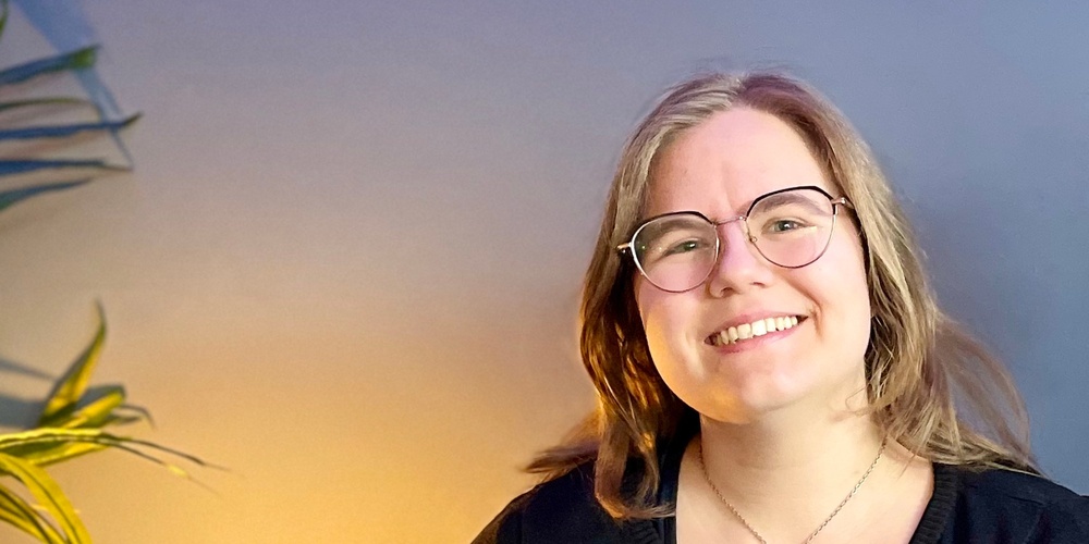 Två leende personer sitter tillsammans i en blå soffa i ett rum med blå vägg och grön växt.