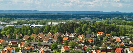 Färgglada villor med röda och gula tak i ett lummigt bostadsområde, omgivna av skog och berg i bakgrunden.
