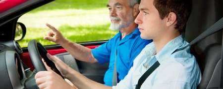 En ung man kör bil med en äldre man som passagerare, troligen under en körlektion.