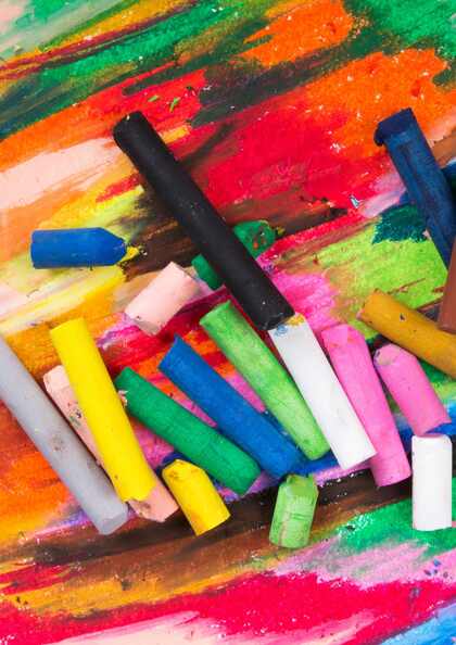 Flera färgglada kritor ligger utspridda på ett papper täckt av färgglada kritstreck.