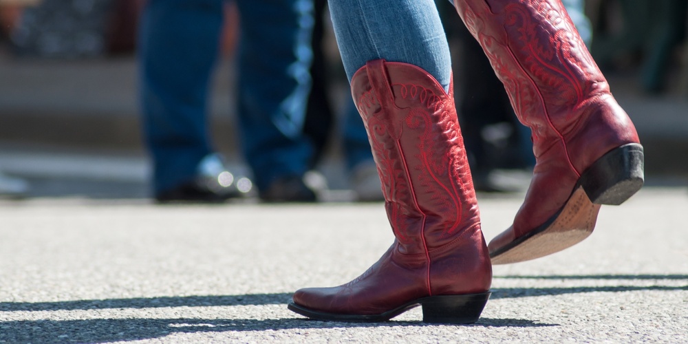 Person i blå jeans och röda cowboyboots dansar utomhus på asfalt.