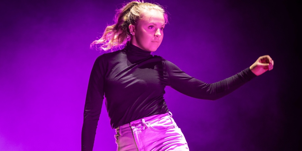 En person dansar barfota på en scen med lila ljus och rökeffekter.
