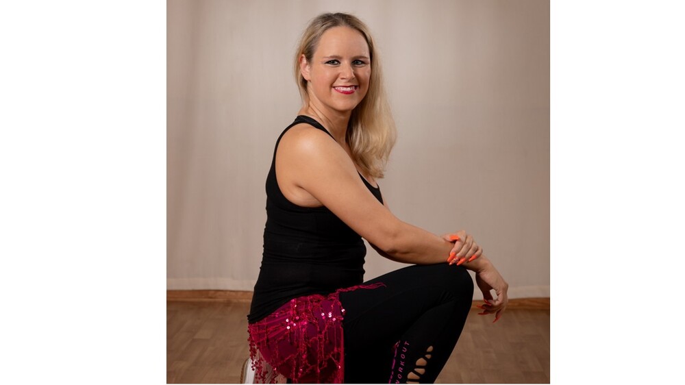 Kvinna sitter på huk i danskläder med röd kjol och svart linne i ett rum med trägolv.