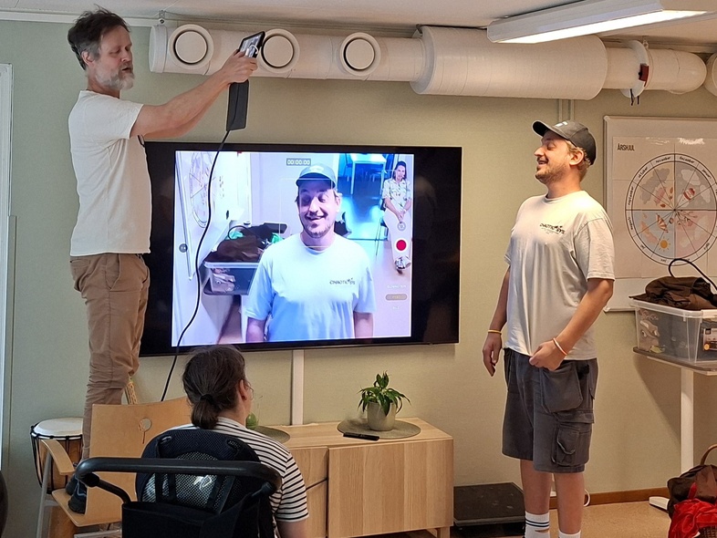 En pedagog filmar en deltagare och en person tittar på