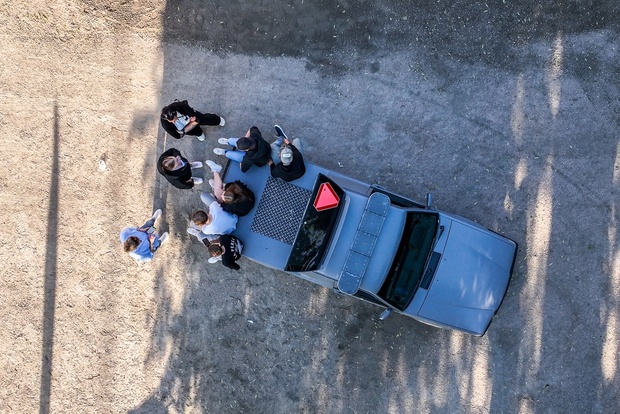 Fågelperspektiv av en grupp människor som står vid en bil på en grusväg.