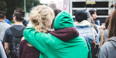 Två personer står tätt tillsammans i en folkmassa, en med grön hoodie har armen om den andra.