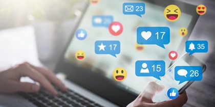 En person använder både en laptop och en smartphone med sociala medie-ikoner och notiser på skärmen.