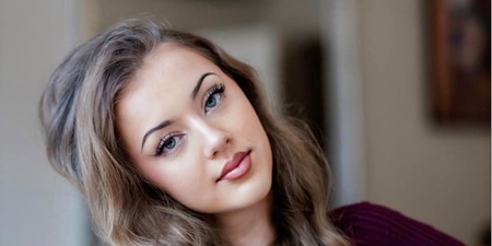 Ung kvinna med långt lockigt hår sitter avslappnat inomhus och tittar mot kameran.