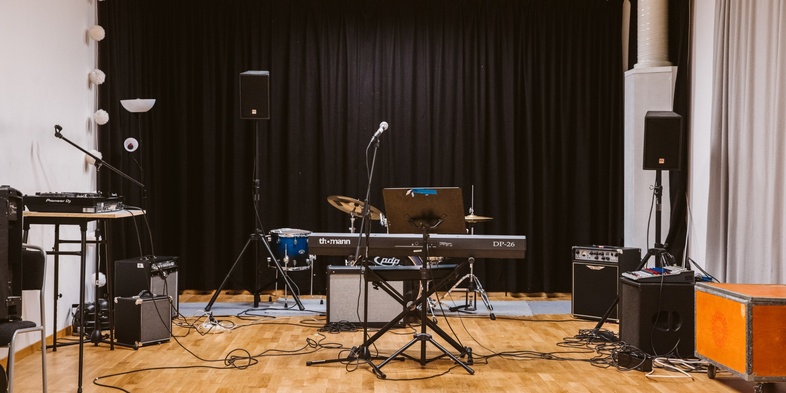 Ett tomt musikrum med instrument som keyboard, trummor, mikrofon och förstärkare på ett trägolv.