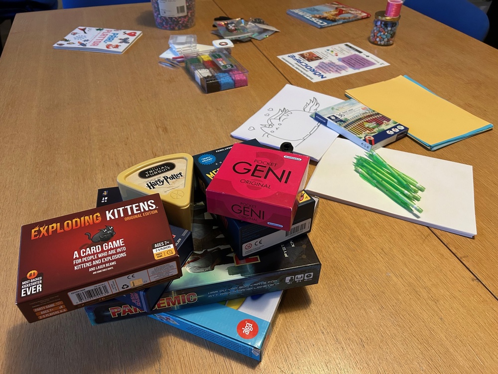 Ett bord med sällskapsspel, kortlekar, papper, pennor och pysselmaterial utspridda.