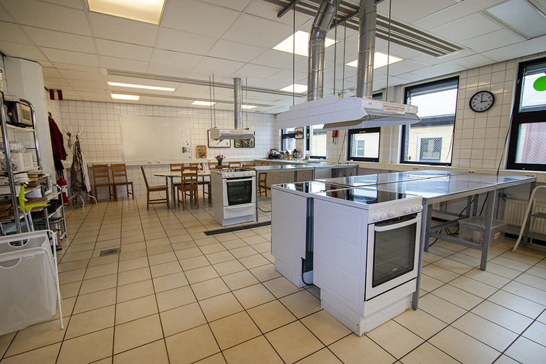 Stort, ljust kök med flera spisar, arbetsytor och matbord, tomt på människor.