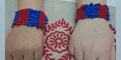 Två barns händer med hemgjorda armband i blått och rött, liggande på en duk med röd brodyr.