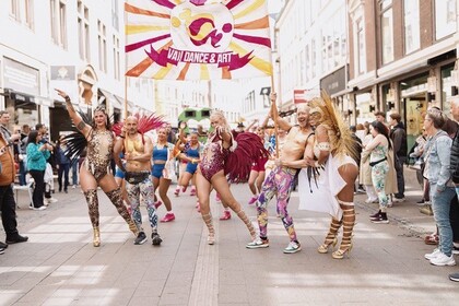 Färgglad dansparad på en stadsgata med utklädda deltagare och publik längs sidorna.