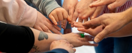 Flera personer sträcker in sina händer mot mitten i en gemensam cirkel, fokus på händerna.