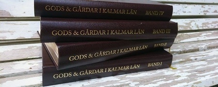 Fyra bruna böcker med titeln 'Gods & Gårdar i Kalmar län' ligger staplade på en sliten träbänk med två prästkragar ovanpå.