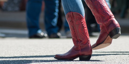 Person i blå jeans och röda cowboyboots dansar utomhus på asfalt.