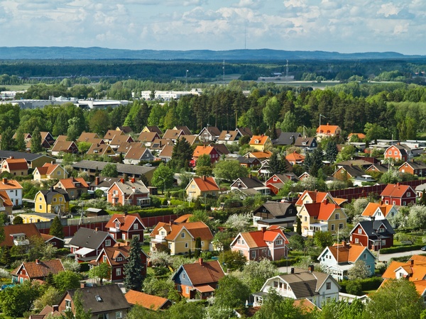 Färgglada villor med röda och gula tak i ett lummigt bostadsområde i Örebro, omgivna av skog och berg i bakgrunden.