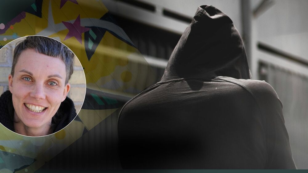 Person i svart hoodie står med ryggen mot kameran i en urban miljö med färgglad bakgrund.