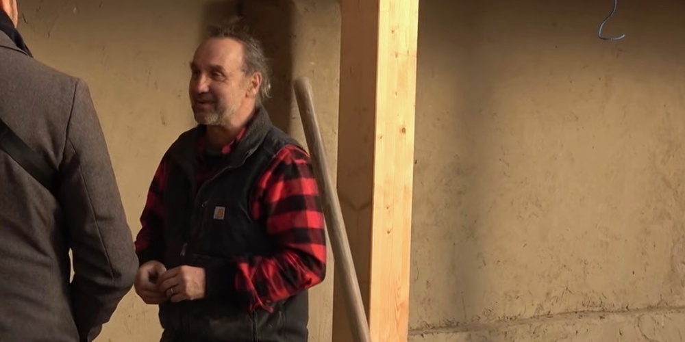 Två personer samtalar inomhus, en bär röd- och svart-rutig skjorta och väst, ansikten är suddade.