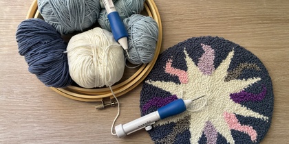 Garnnystan, broderiram, punch needle-verktyg och ett färdigt tuftat rundel med solmotiv på ett träbord.