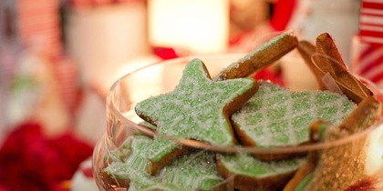 En skål med gröna stjärnformade kakor dekorerade med socker, omgiven av juldekorationer.