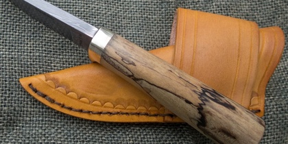 En kniv med trähandtag och damaskerat blad ligger på ett grönt tyg bredvid ett brunt läderfodral.