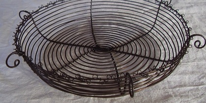 En rund korg av svart metalltråd med spiralformad botten och dekorativa öglor längs kanten.