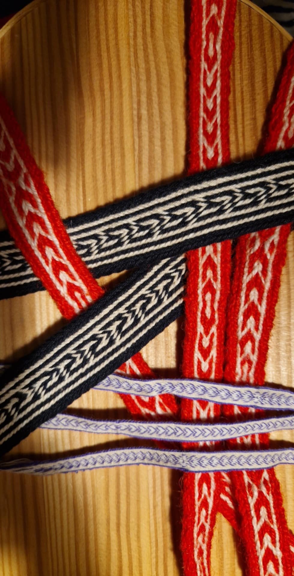 Flera färgglada band i rött, svart och vitt samt lila ligger korslagda på en träyta.